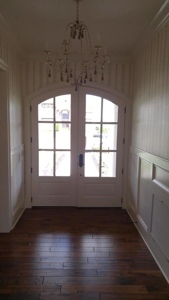 White double doors with arched tops, chandelier, and wood floor hallway.