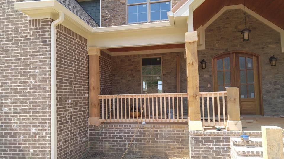 Brick house exterior with porch, wooden columns, and railing.