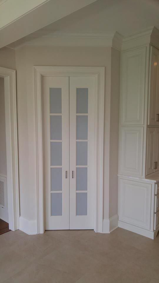 White double doors with glass panels and white trim, set in a corner of a room with white cabinets and beige floor tiles.