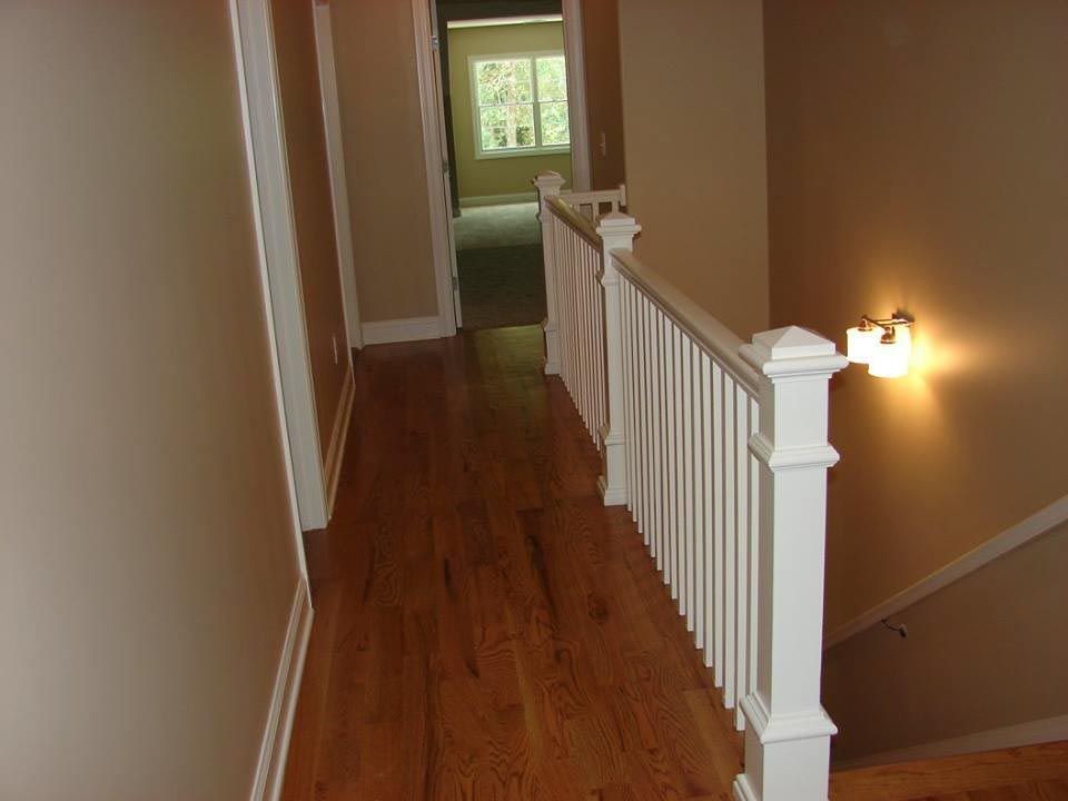 Hallway with hardwood floor, white railing, and beige walls.
