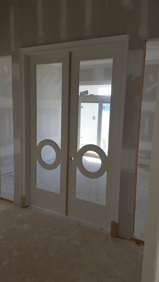 White double doors with circular cutouts and frosted glass, in a room under construction.