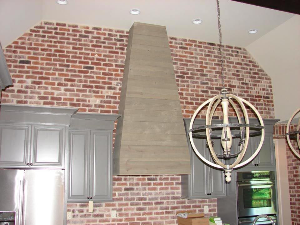 Kitchen with gray cabinets, brick wall, concrete range hood, and globe light fixture.