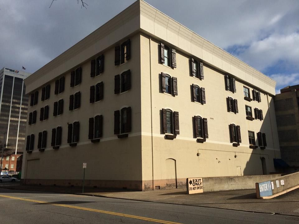 Tan building with dark shutters on a city street; overcast sky.
