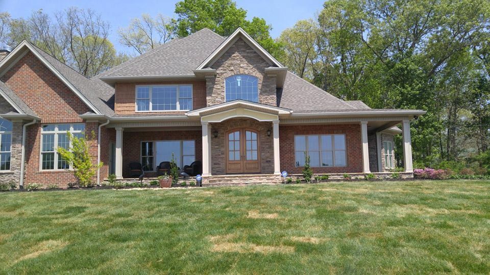 Large brick and stone house with a covered porch and green lawn on a sunny day.