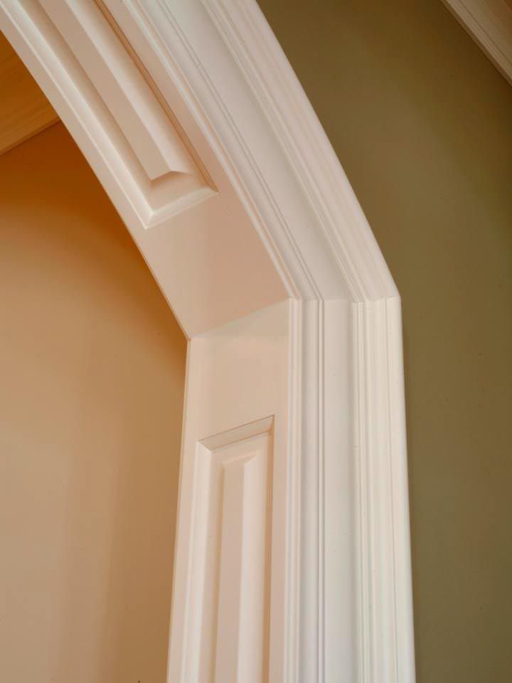 White, decorative door frame with detailed molding against light and olive green walls.