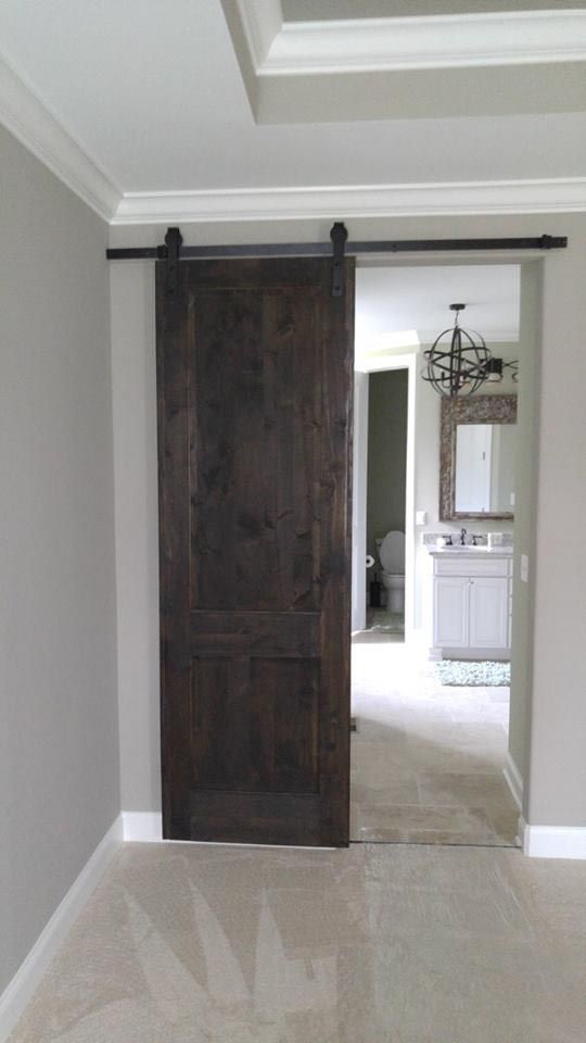 Dark stained wooden barn door open, leading to a bathroom. Beige carpet, gray walls, white trim.