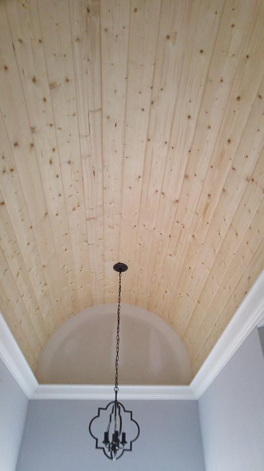 Wooden plank ceiling with a chandelier in a room with a gray wall and white trim.