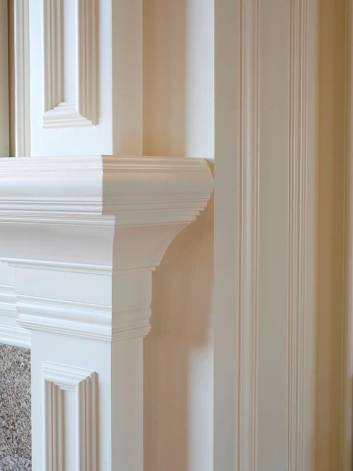 Close-up of white decorative trim on a fireplace mantel, with a light-colored wall featuring vertical paneling.