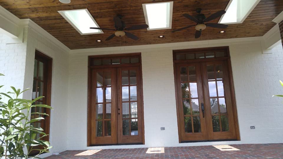 Back patio with wood double doors and a single wood door. The home is white with two fans and wood paneling on the ceiling.