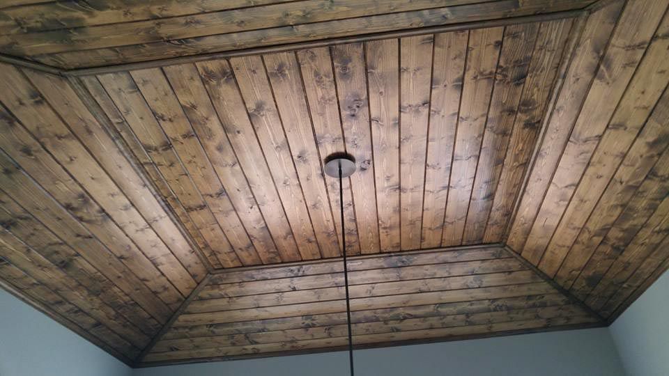 Wooden plank ceiling with a central light fixture, stained in shades of brown.