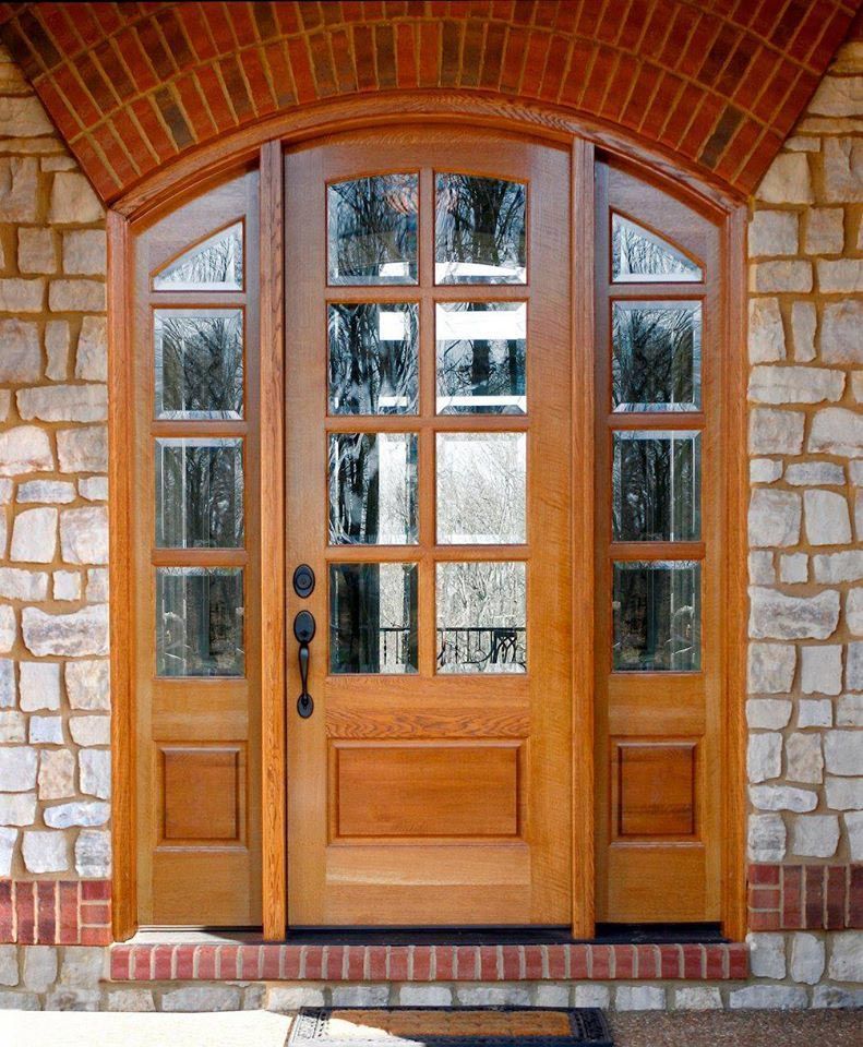 Exterior arched wood door with glass paneling and windows on both sides.