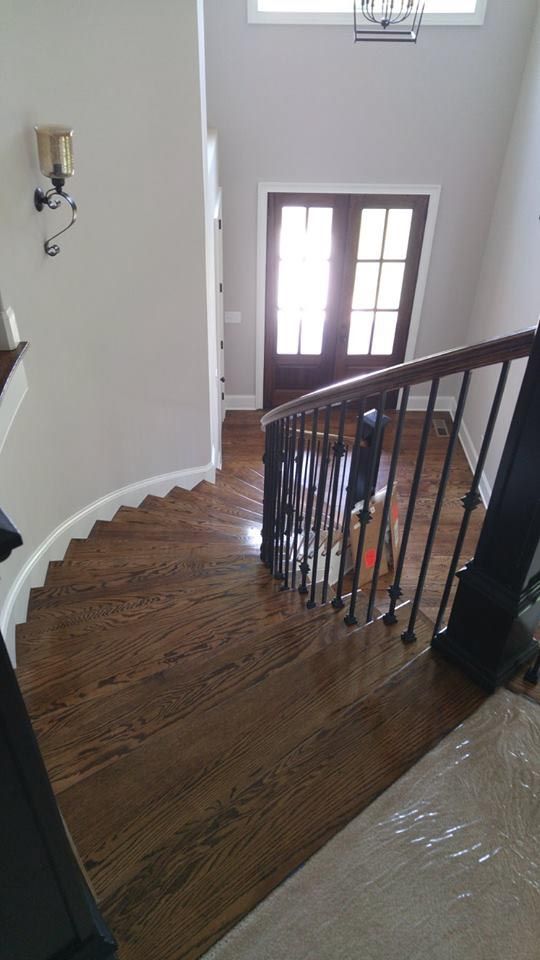 A wooden staircase with dark railing leads to a front door with light streaming in.