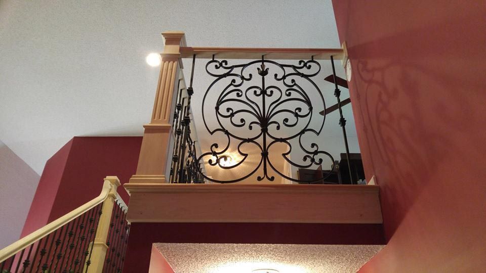 Ornate black ironwork railing on a balcony, beige pillars, red and light pink walls.