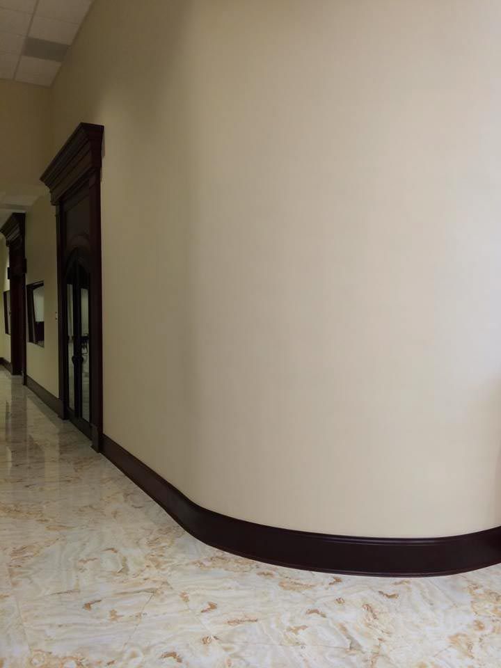 Curved off-white wall in a hallway with dark wood trim and marble flooring.