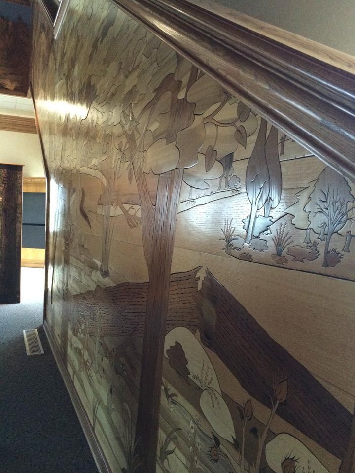 Wooden staircase wall with inlaid landscape design, various wood tones.