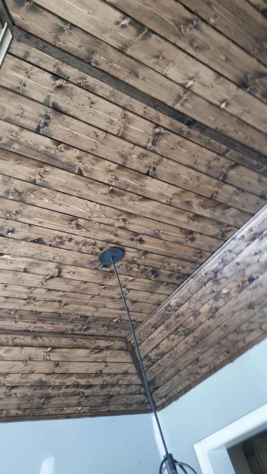 Wooden plank ceiling with dark stain and a black pendant light.