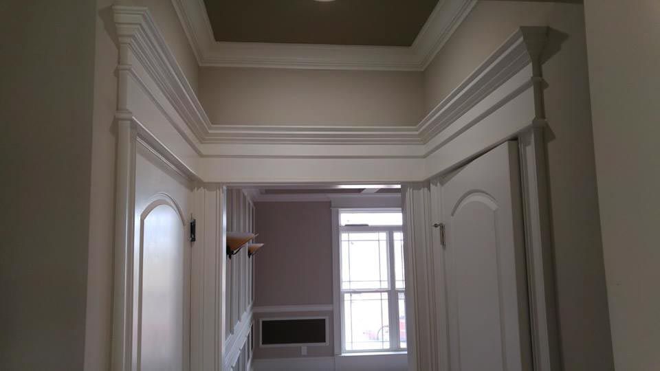 Hallway with ornate white trim around doorways and opening to a room with a window.