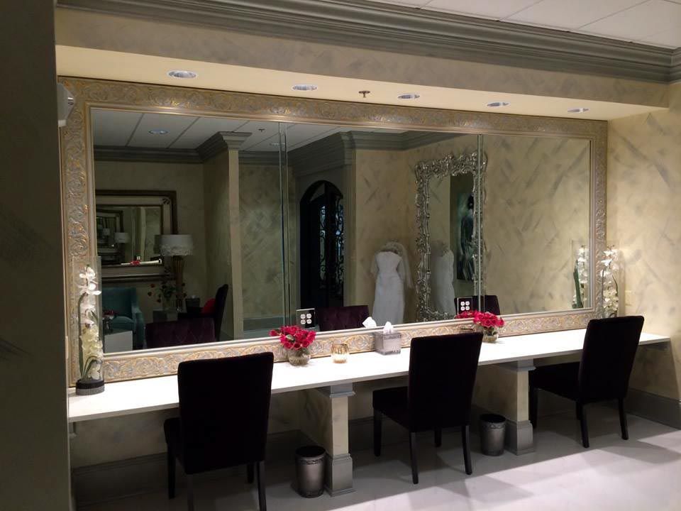 Vanity area with large mirrors, marble countertops, black chairs, and floral arrangements.
