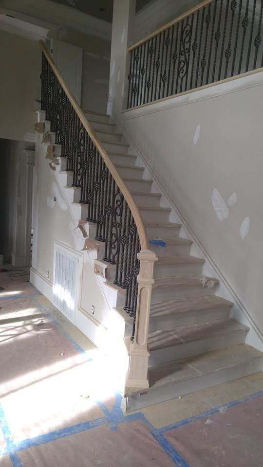Staircase with wooden steps and railing, black iron balusters, light beige walls, and tan colored stair treads.