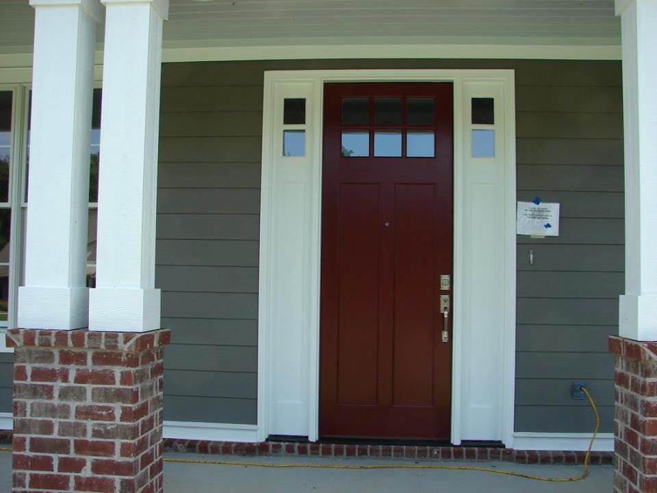 Entrance to a grey home with two basic columns and a wood door with three window panes.