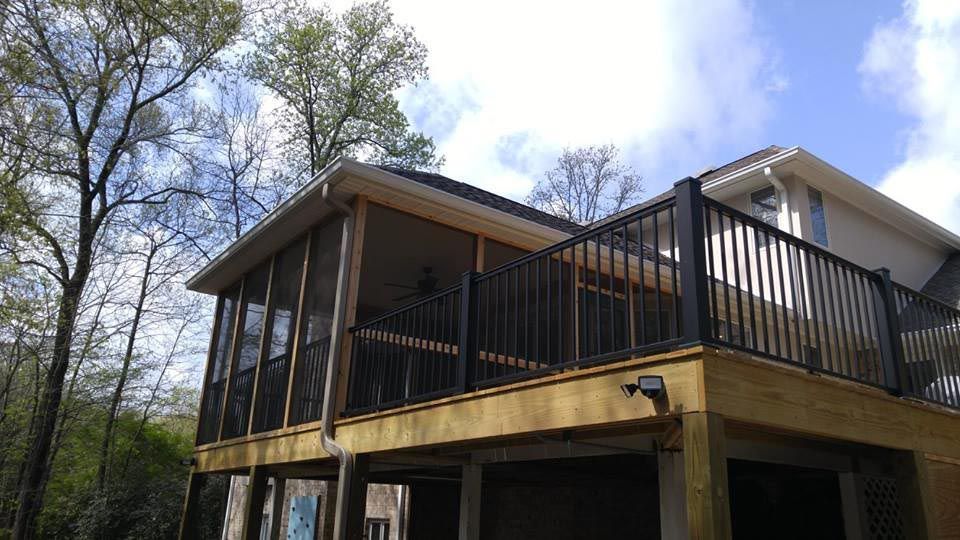 Back of a home with a large open deck with black rails and a large screened in porch.