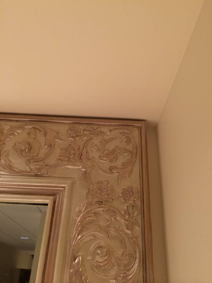Ornate, ivory-colored mirror frame against a beige wall and ceiling.