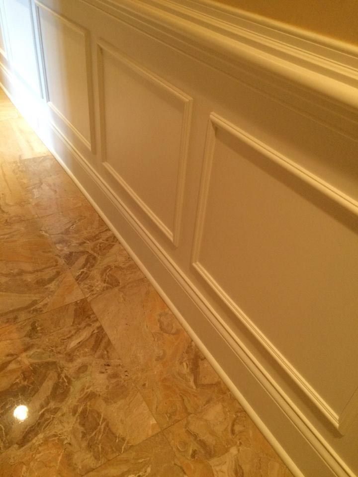 Cream-colored paneled wall with decorative molding on a polished marble floor, illuminated by natural light.