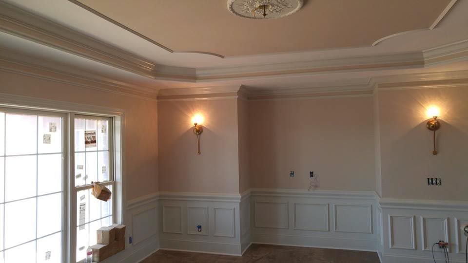 Interior room with white walls, wainscoting, sconces, and crown molding. Unfinished window and ceiling detail.