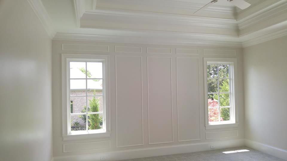 White bedroom with two windows flanking a paneled wall; white crown molding, ceiling trim.