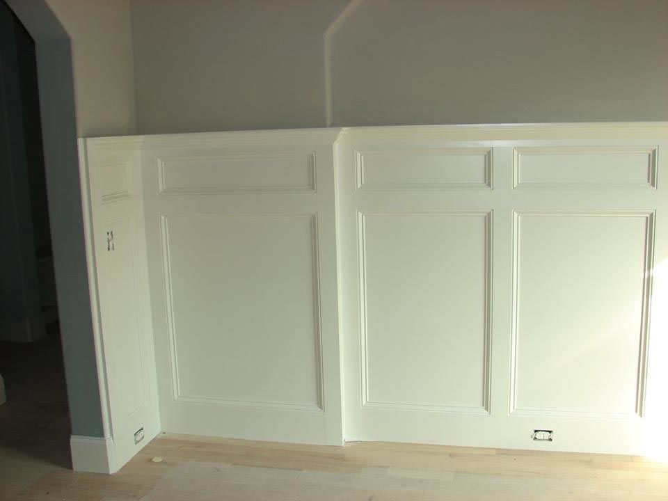 White wainscoting on a wall with detailed rectangular panels. Gray and light-colored walls and floor.