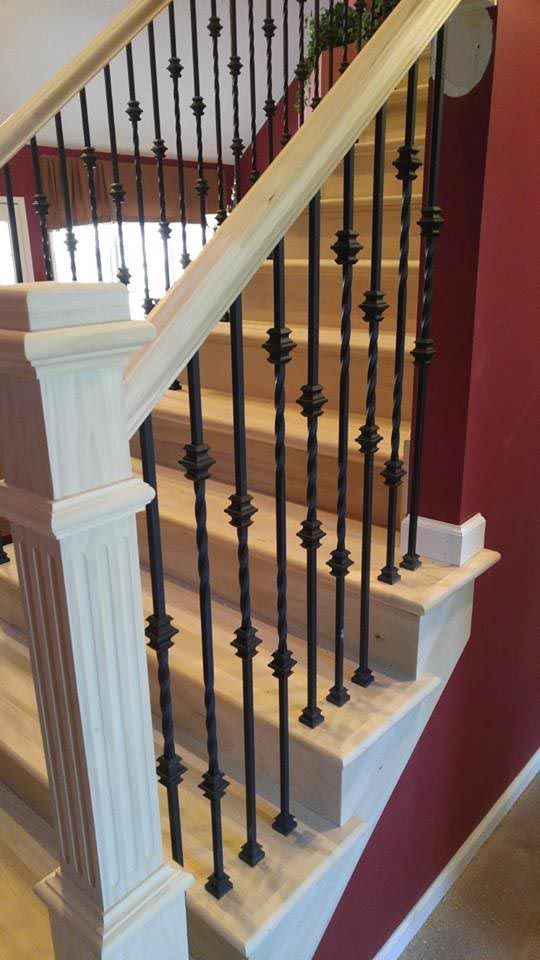 Staircase with light wood steps, white newel post, dark metal balusters, and a light wood handrail.