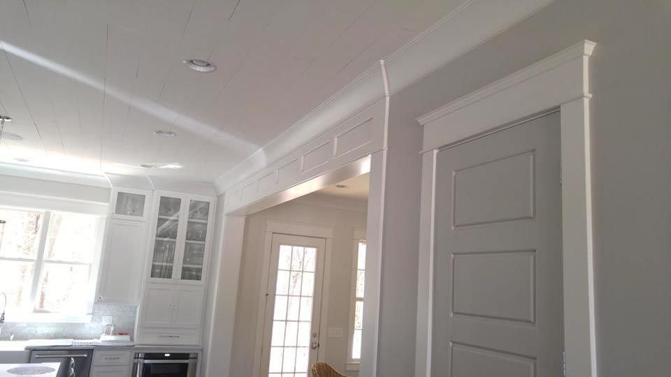 Interior view of white trim around a doorway and ceiling, with a kitchen visible in the background.