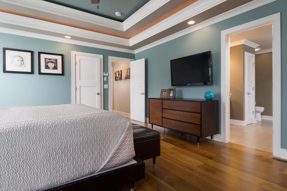 Bedroom with blue walls, wood floor, and a TV above a dresser. A bed is in the foreground.