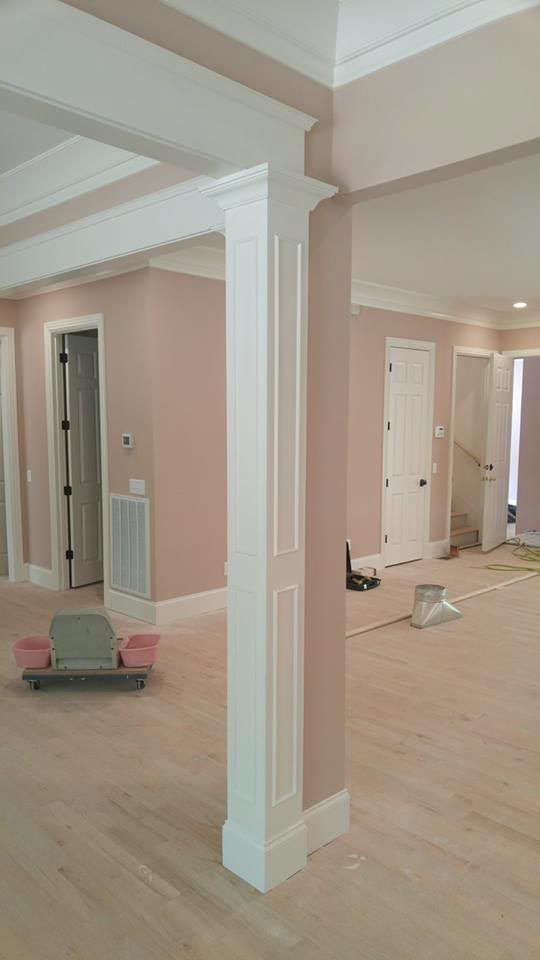Interior with painted pink walls, white trim and columns, and unfinished light-colored wooden floors.