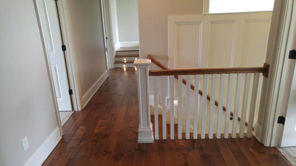 Hallway with hardwood floor, stairs with white railing, doors on either side, and sunlight at the end.