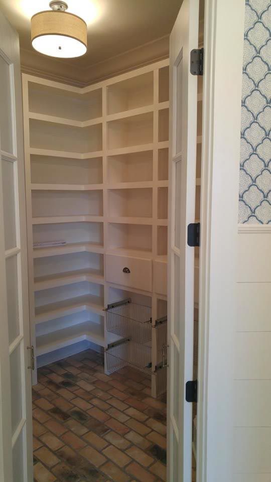 Corner pantry with white shelves and brick floor, viewed through open French doors.