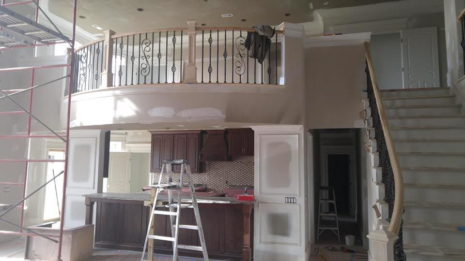 Interior under construction: two-story space with a staircase, balcony with ornate railing, and kitchen cabinetry.
