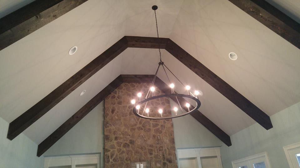 Vaulted ceiling with dark wood beams, a circular chandelier, and a stone fireplace.