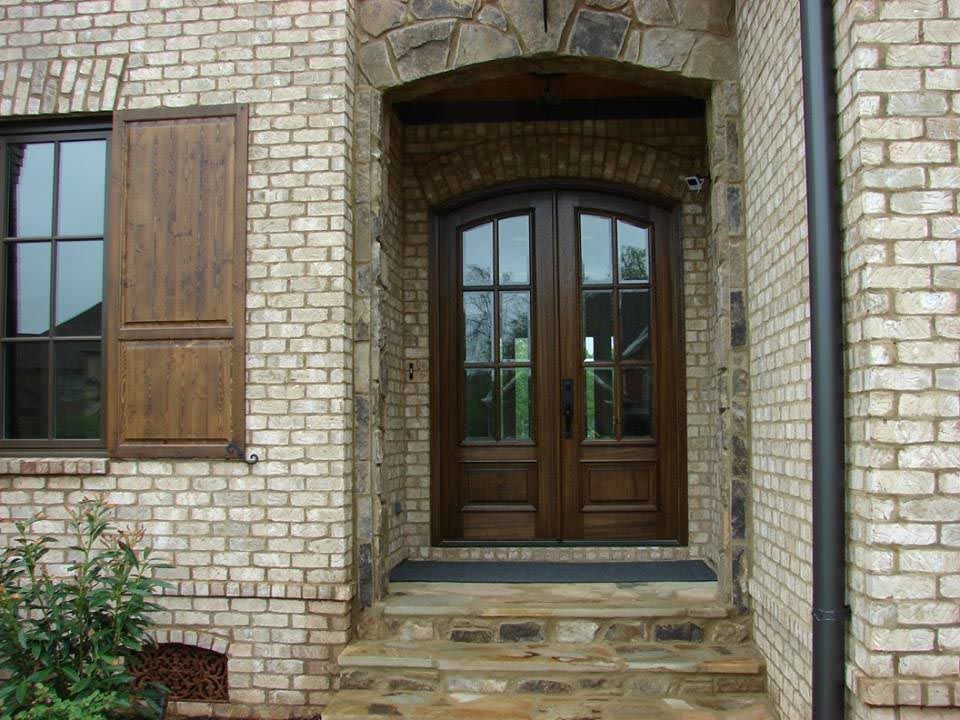 Exterior view of a home with brown double doors, brick exterior, stone archway, and window with shutters.