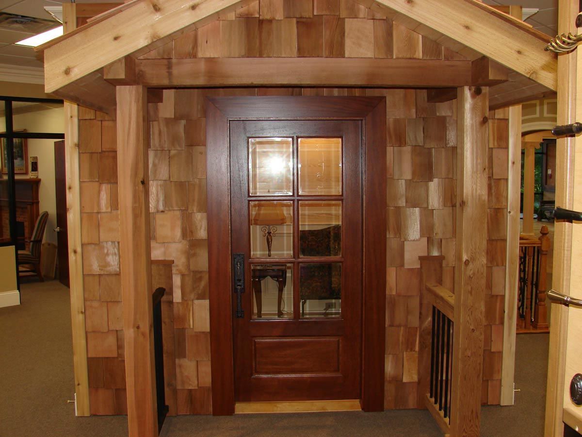 Wooden entry door with glass panes and cedar shingle siding.