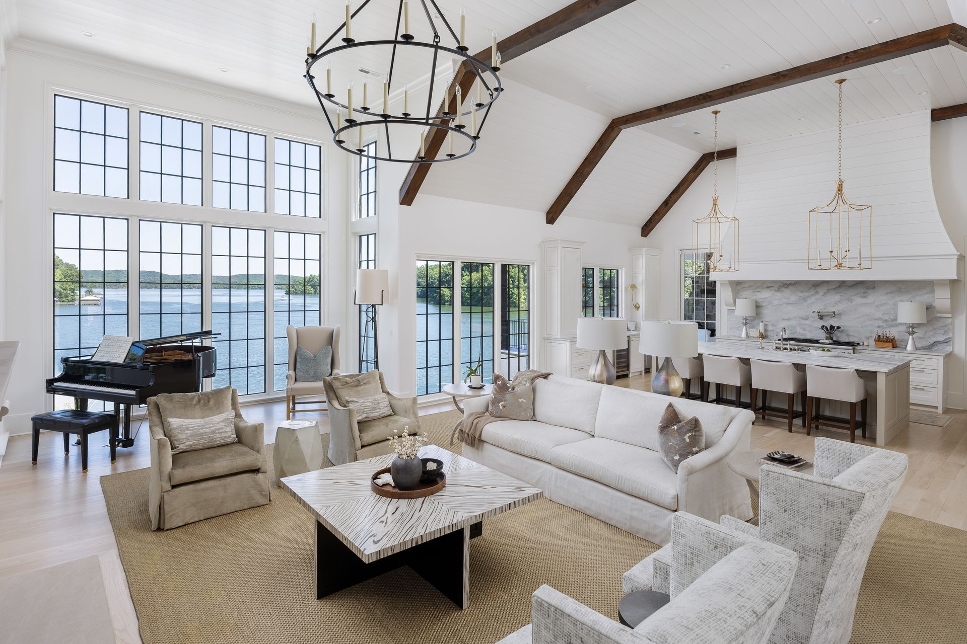 Bright open living room with white sofa, fireplace, piano, and large windows overlooking water