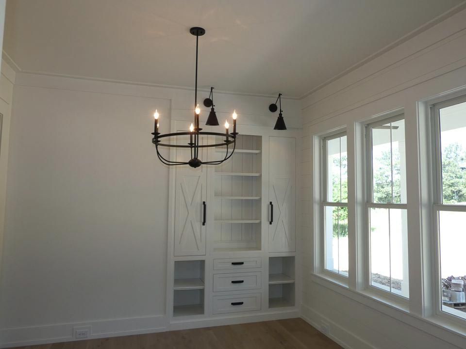 White dining room with a chandelier, built-in shelving, and windows.
