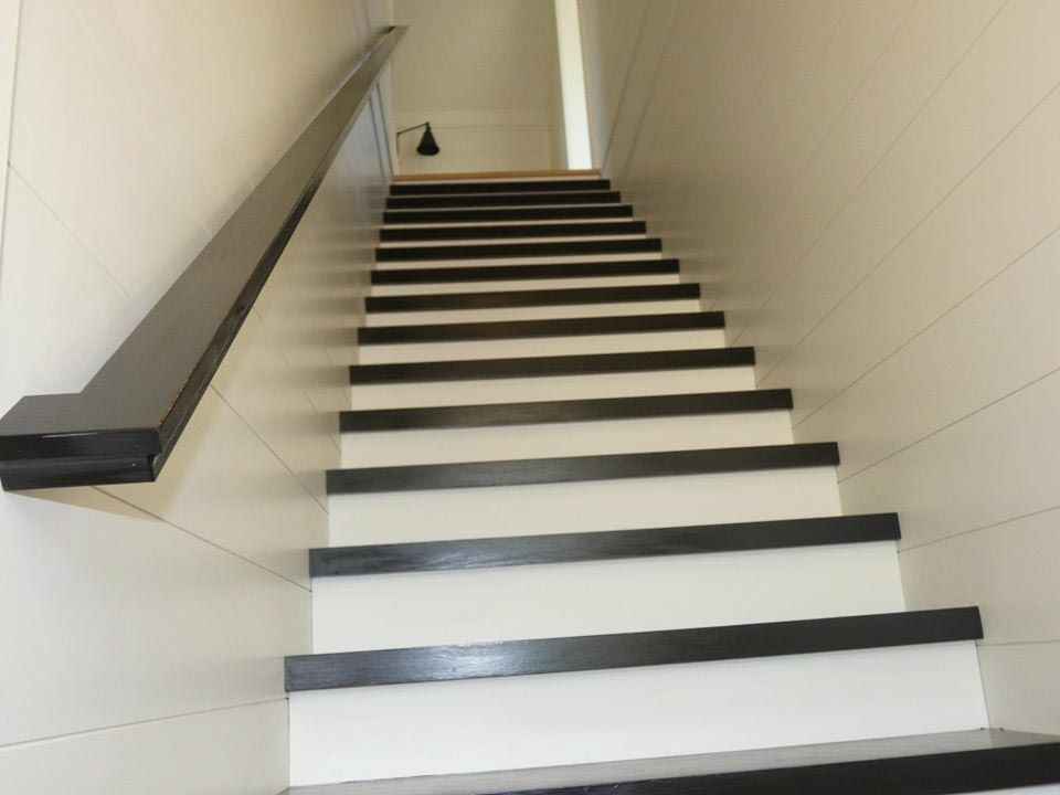 Staircase with white risers and dark treads, leading upwards. Dark handrail on the left.