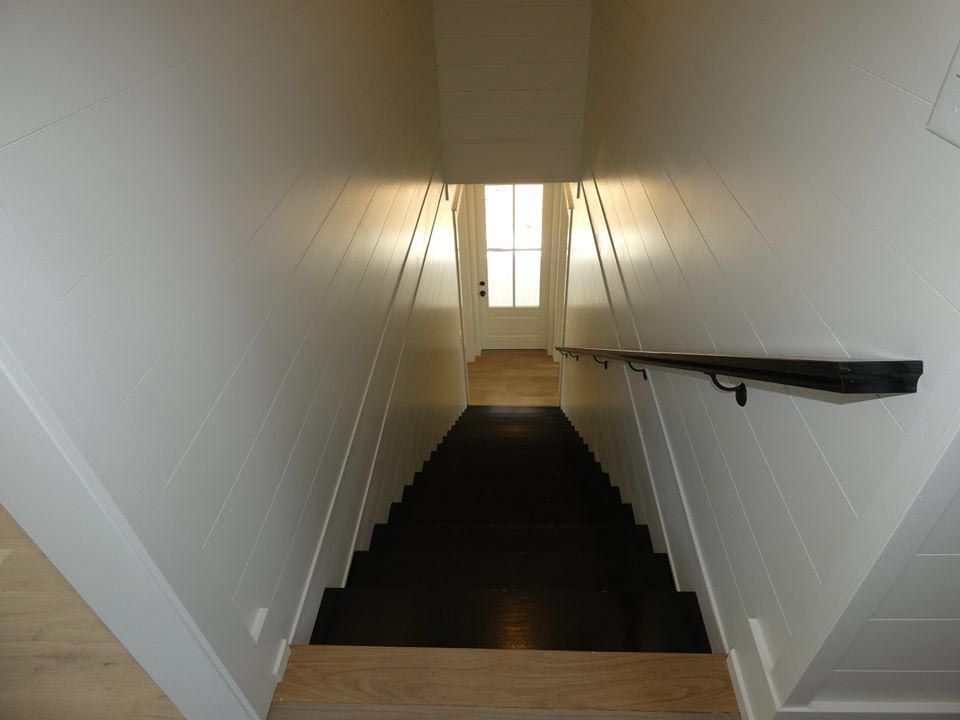 Staircase with black treads, white walls, and a black handrail, leading to a door with sunlight.