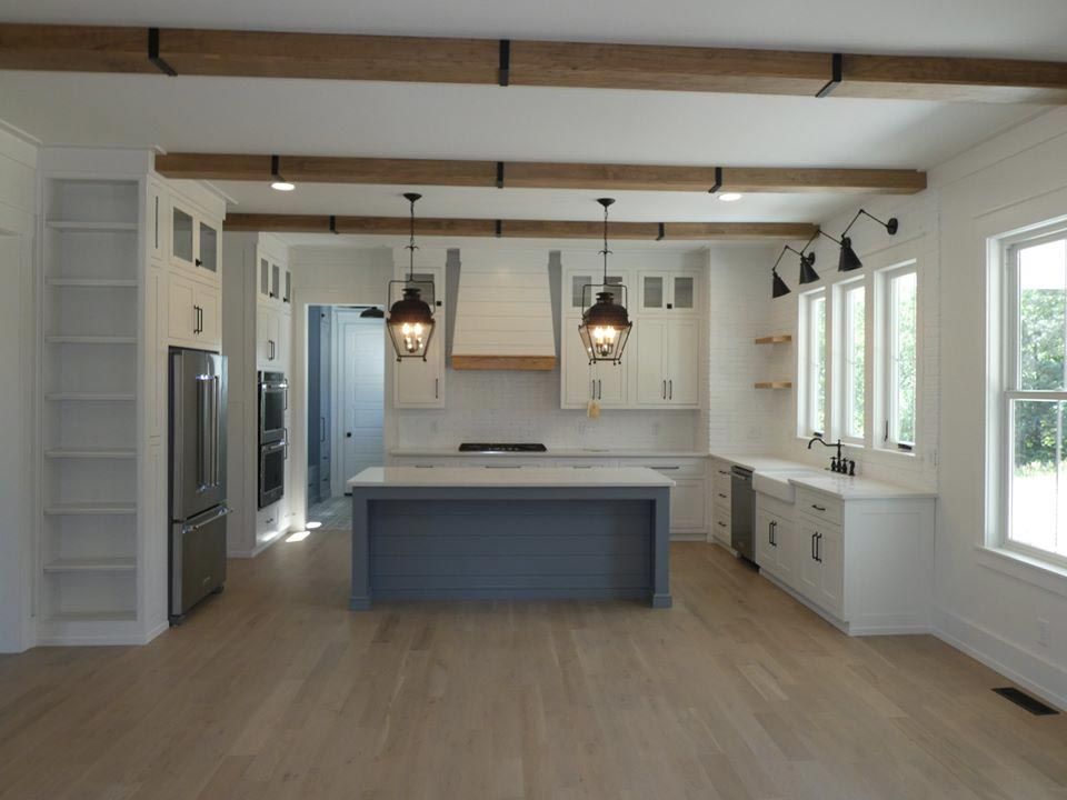 Modern kitchen with white cabinets, blue island, wood beams, and stainless steel appliances.