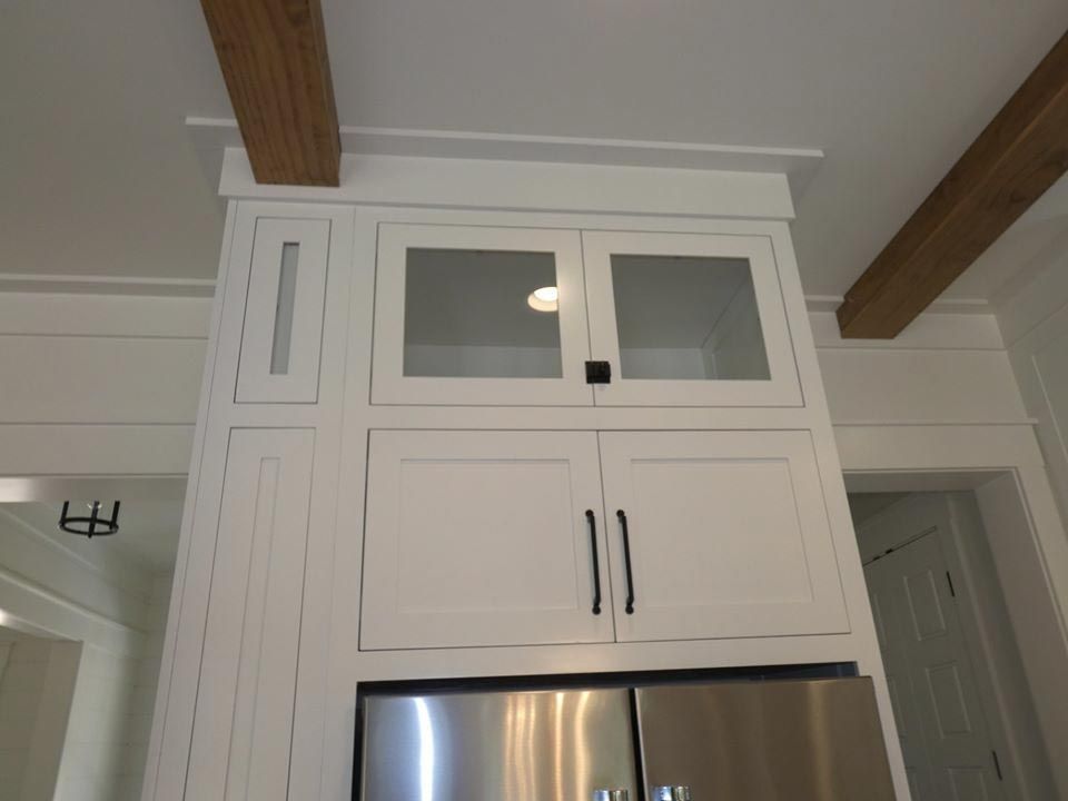 White kitchen cabinets above a stainless steel refrigerator, with glass-fronted upper cabinets.