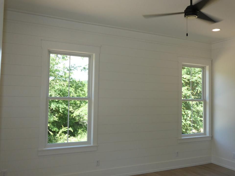 Two white framed windows on a white paneled wall, with a ceiling fan.