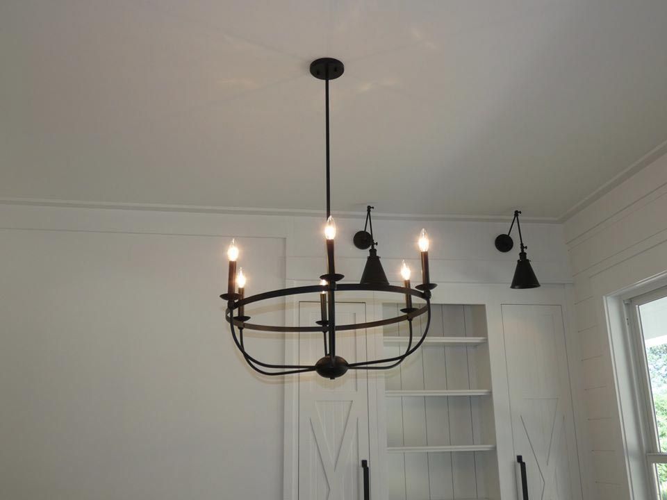 Black chandelier hanging from a white ceiling. White cabinetry and sconces are visible.