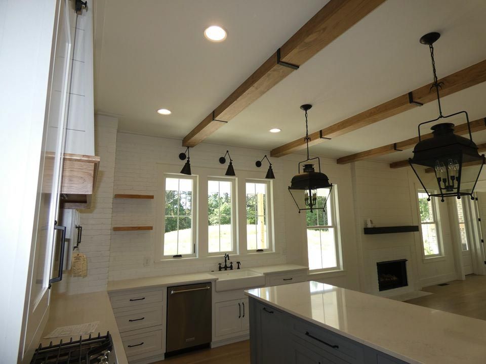Kitchen with white cabinets, windows, beams, and pendant lights.