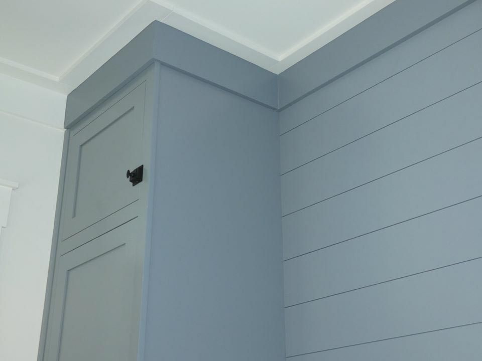 Corner cabinet and shiplap wall painted gray, with white crown molding.
